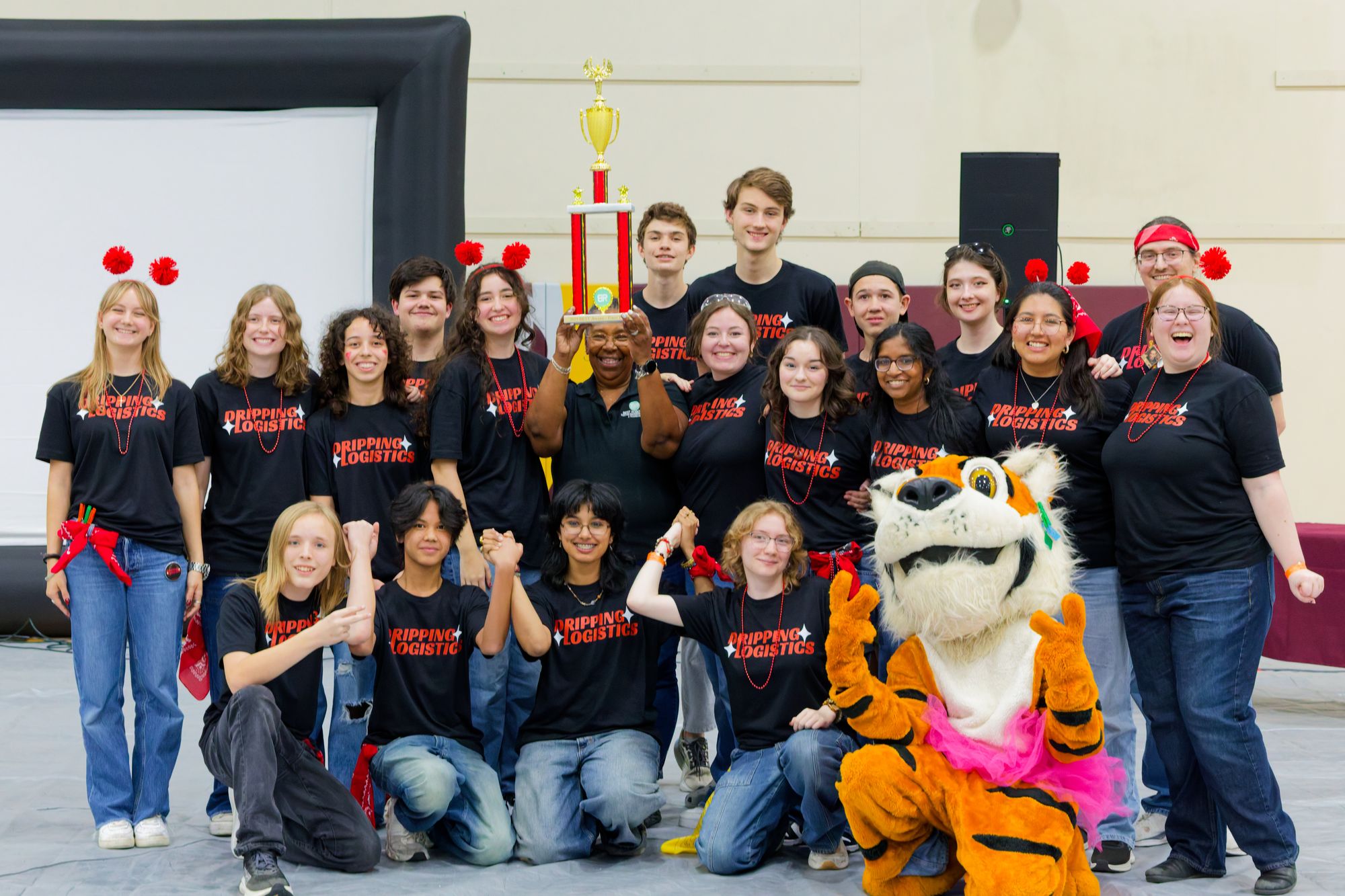 The Dripping Logistics team in matching black shirts holding up a trophy, with the school tiger mascot kneeling in front