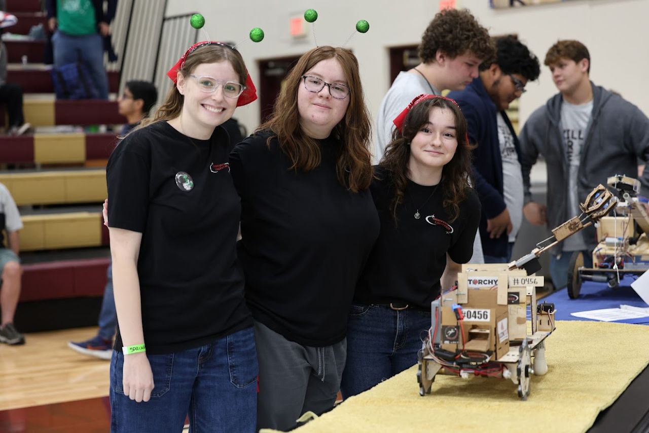 Three team members posing next to their cardboard robot at competition