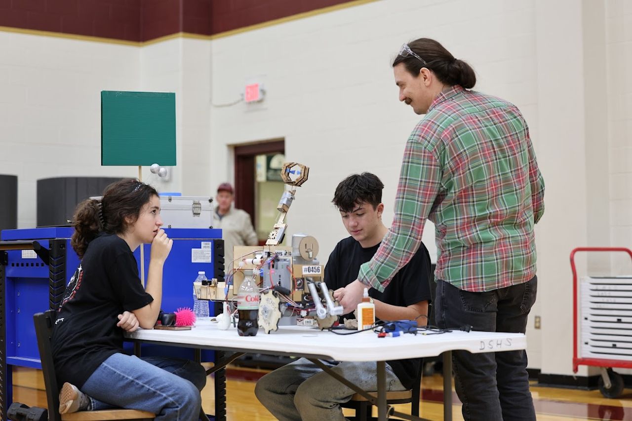 A mentor and two students working on the robot at the DSHS pit table