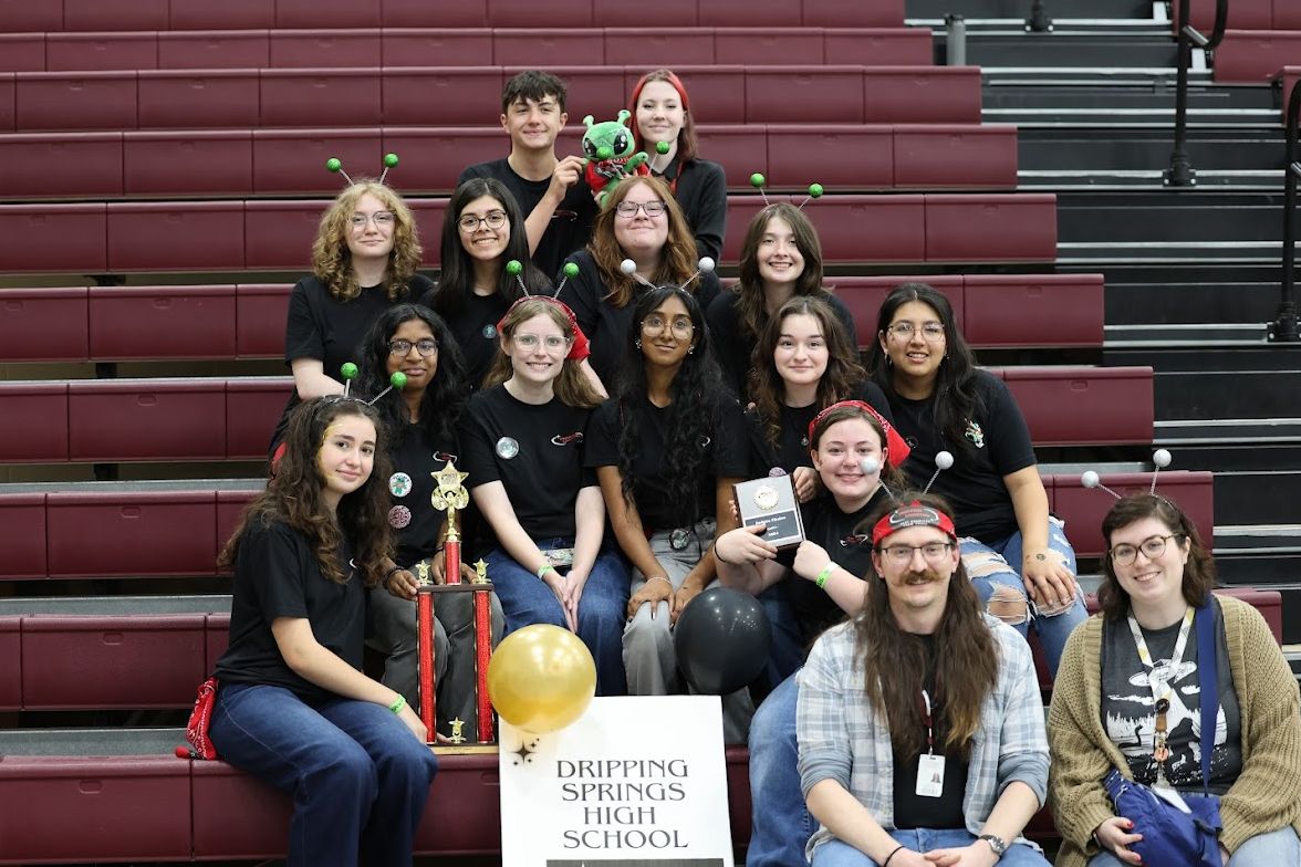 The team seated in the bleachers with a trophy, plaque and mascot