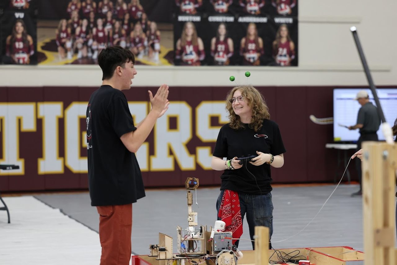 A driver holding a controller and smiling at a teammate next to the game field